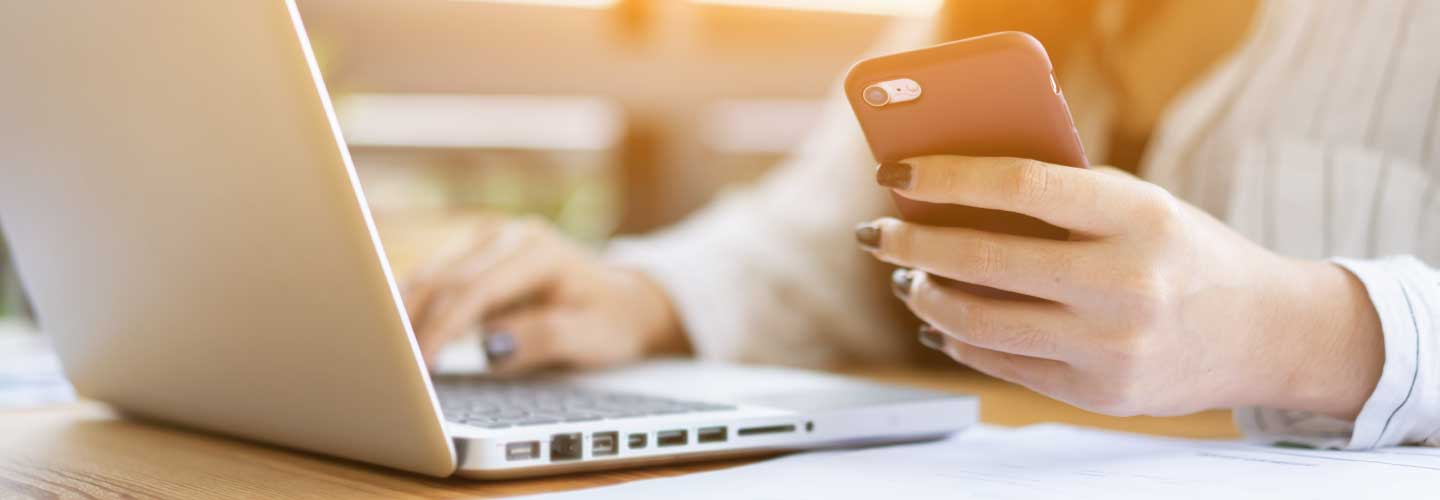 person working on laptop and holding a mobile phone
