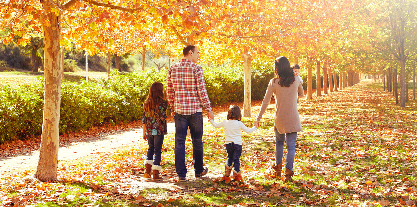 Family of 5 walking in a park with fall leaves.