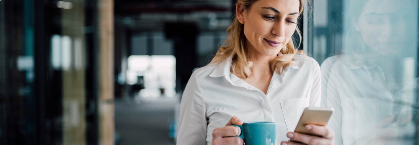 A businesswoman holding a mug and a smartphone.