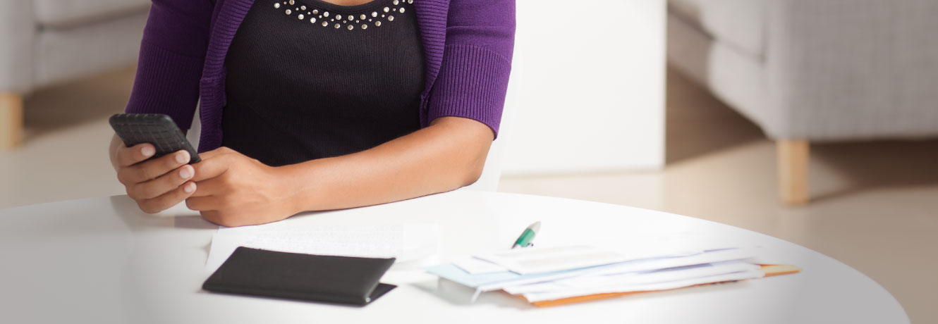 Woman holding mobile phone with checkbook and bills on a round table.