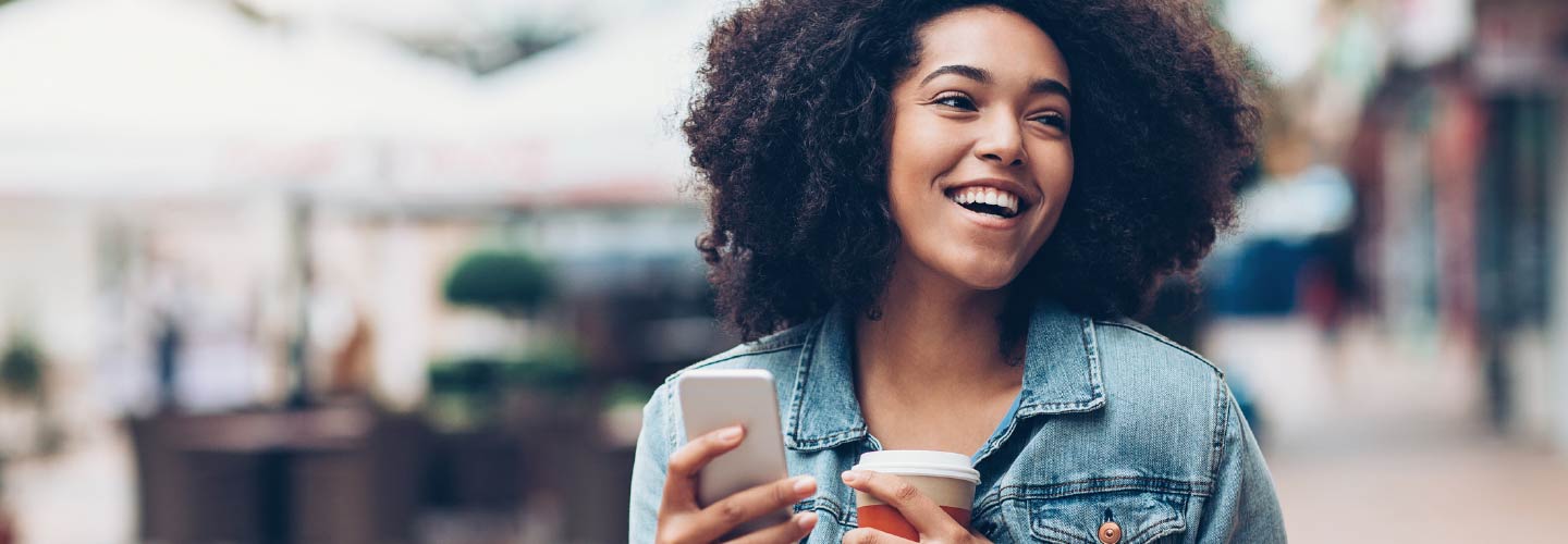 A woman holding a coffee cup and a smartphone.