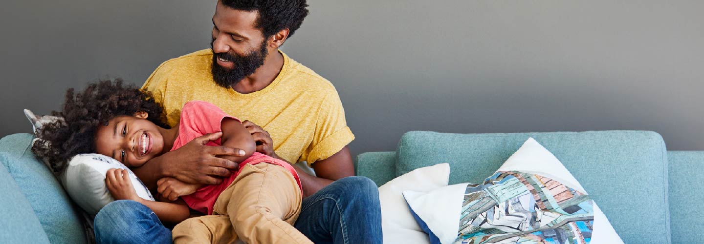 A dad and his young child playing together on a couch.