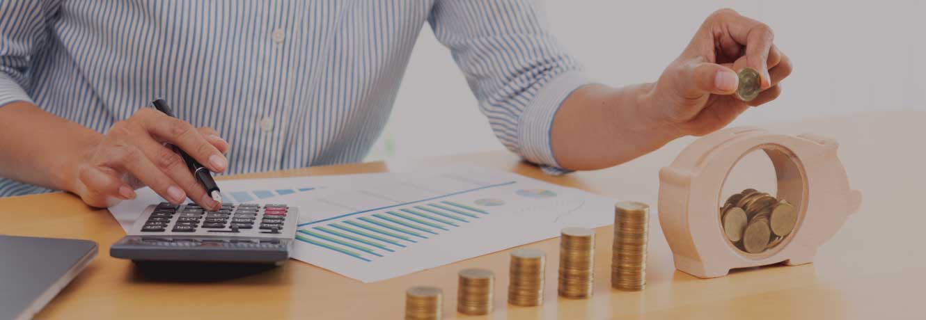 Woman dropping coins into a wooden piggy bank while pushing buttons on a calculator.